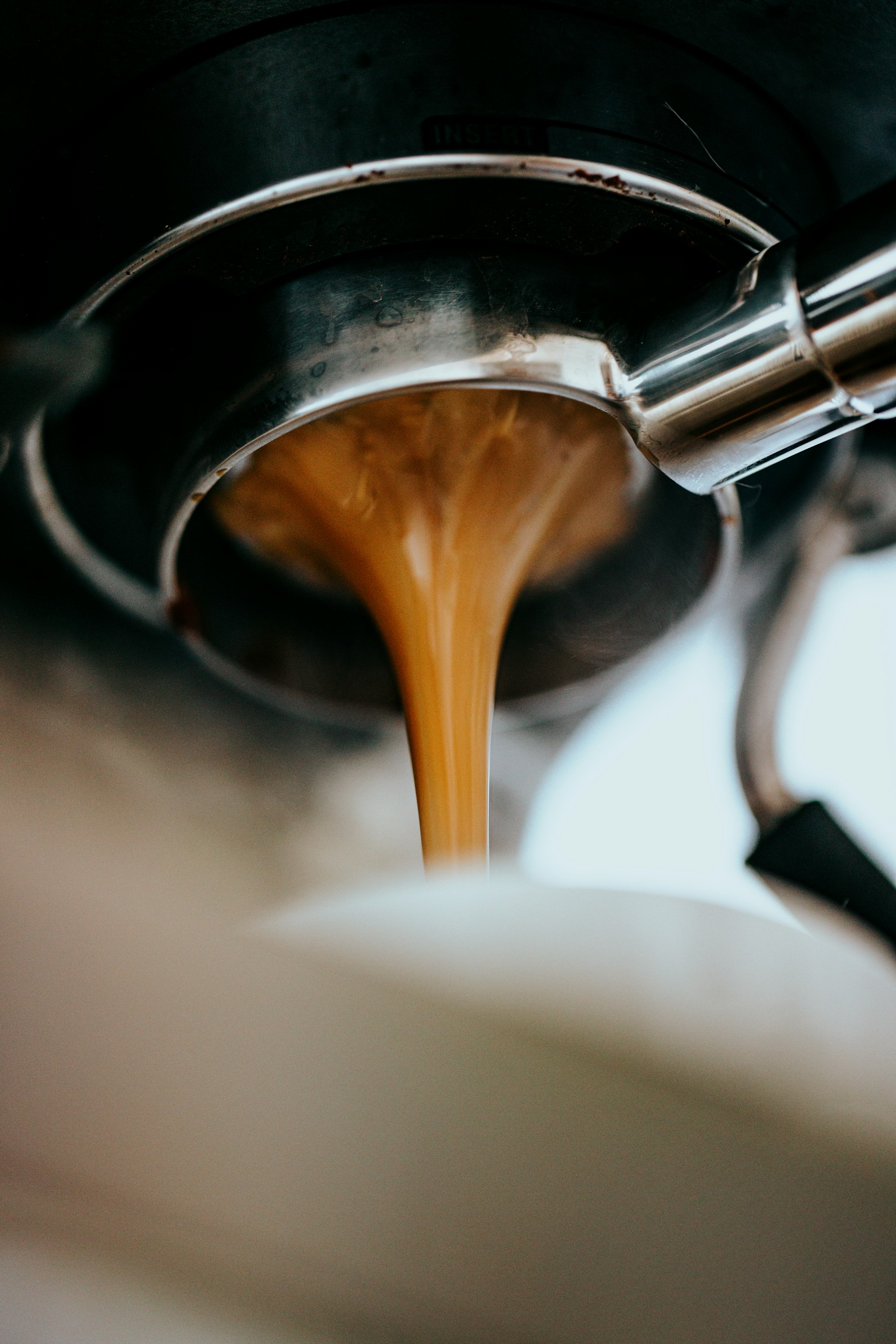 Espresso coulant d'un porte-filtre dans une tasse blanche.